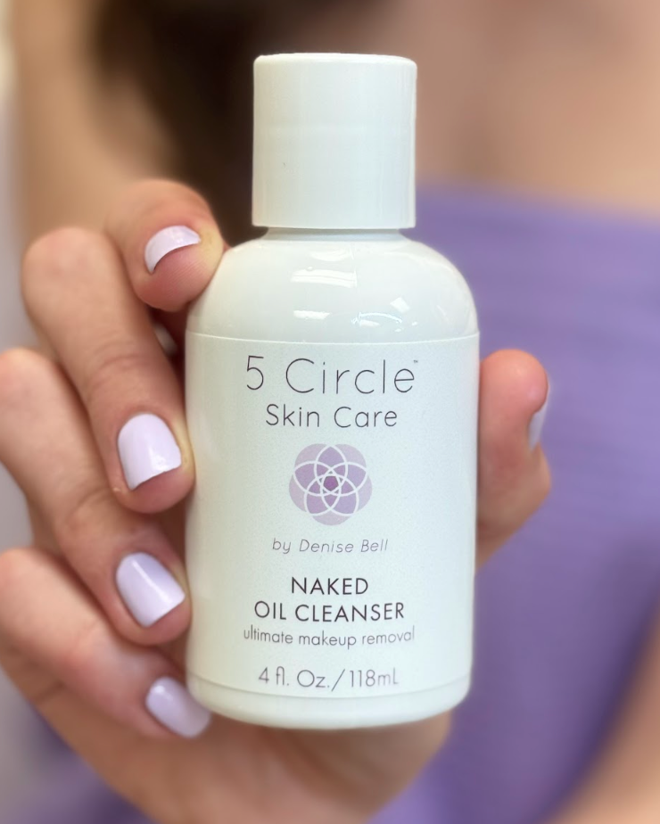 5 Circle Skin Care Naked Oil Cleanser in their hand, with a purple towel draped behind them in a softly lit indoor setting.