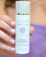 A hand with lavender nail polish holds a white bottle of 5 Circle Skin Care Glacial Moisturizer against a soft purple and beige blurred background.